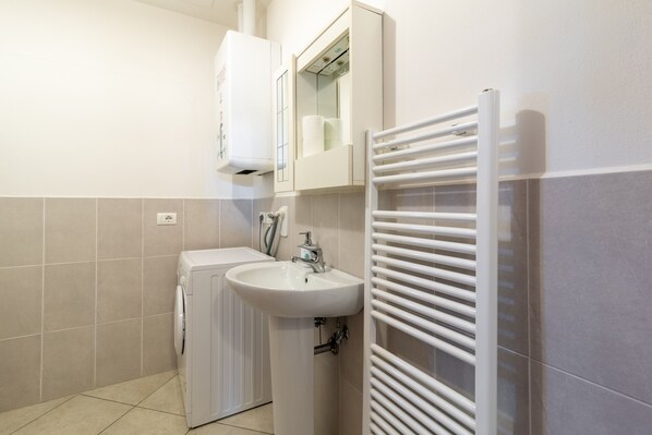 A bathroom with a washing machine, a sink, and a towel rack.