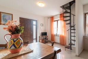 Ein Essbereich mit einem Holztisch, einer bunten Vase, einem Fernseher und einer Wendeltreppe.