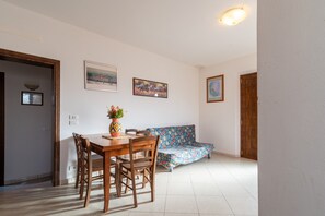Een eetgedeelte met een houten tafel en stoelen, een bloemenbank en ingelijste foto’s aan de muur.