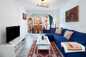 A living room with a TV, sofa, coffee table, and dining area with chairs and a table.