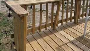 Una terraza de madera con barandilla que da a una playa y el agua.