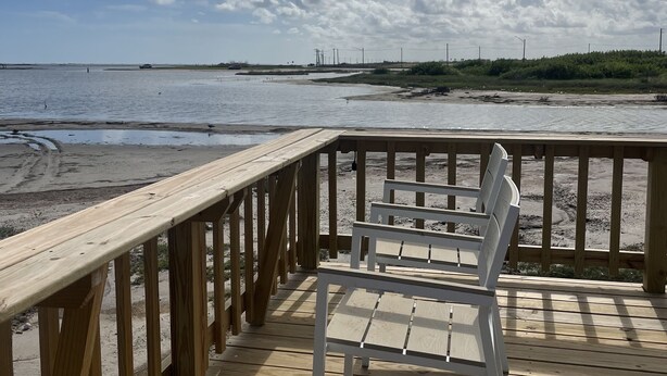 Una terraza de madera con una mesa y sillas blancas que da a una playa.