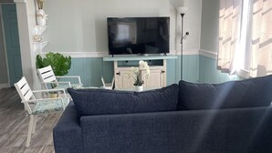 Una sala de estar con un sofá azul oscuro, un televisor de pantalla plana, un ventilador de techo y suelo de madera.