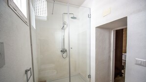 Un baño con ducha envuelta en vidrio, un lavamanos blanco y una puerta visible que conduce a otra habitación.