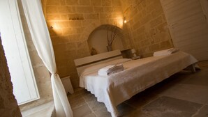 Habitación de paredes de piedra con una cama, una cortina blanca y una puerta.