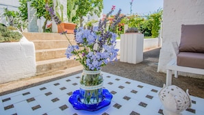 Un área de estar al aire libre con una mesa de baldosas y un jarrón azul con flores.