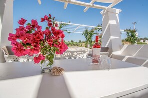 Une table blanche ornée d’un vase de fleurs roses, d’un coquillage et d’une bouteille.