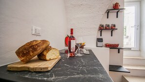 A kitchen counter with bread, a wine bottle, and a glass. There are shelves with jars and a teapot.