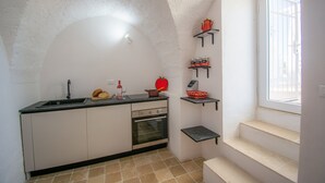 A kitchen with a sink, oven, and shelves with kitchen items.