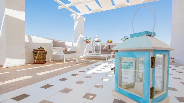 A sunlit outdoor seating area with a white pergola, a blue lantern, and potted plants.