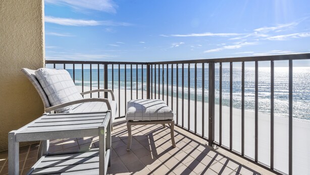 Een balkon met twee stoelen en een tafeltje, met uitzicht op het strand.