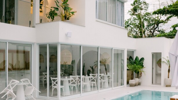 Uma casa moderna de dois andares com piscina, móveis brancos e plantas em vasos.