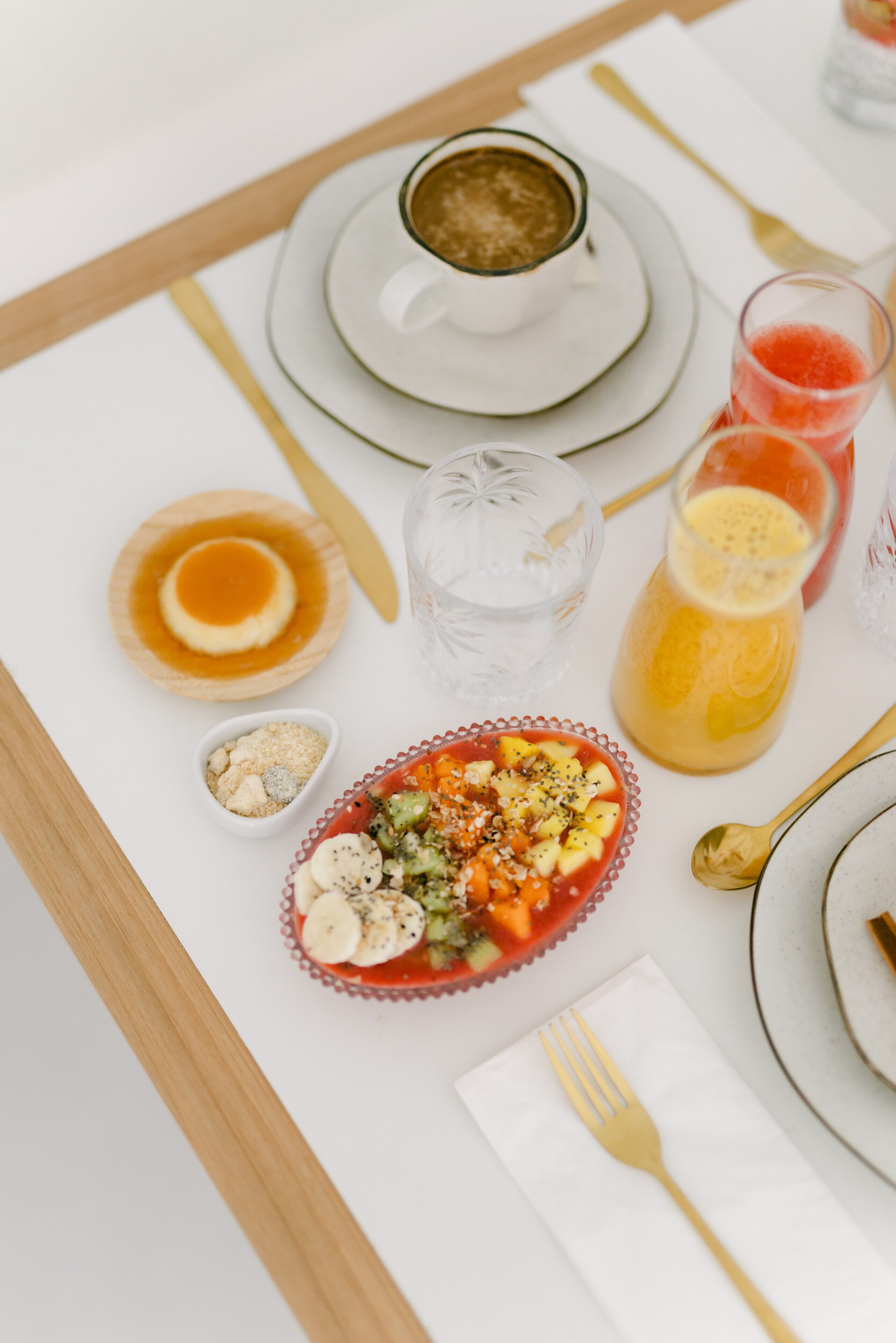 Una mesa de desayuno con una taza de café, un vaso de jugo de naranja, un vaso de agua, un plato de fruta y un tazón pequeño de nueces.