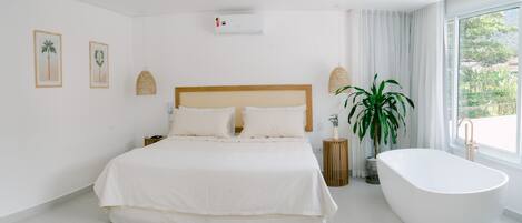 Un dormitorio moderno con una cama grande, una bañera independiente y un ventanal con vistas a zonas verdes.