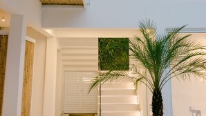 Interior moderno com escada que leva a um segundo andar, uma grande palmeira em vaso e guarda-corpo de vidro com vista para o espaço.