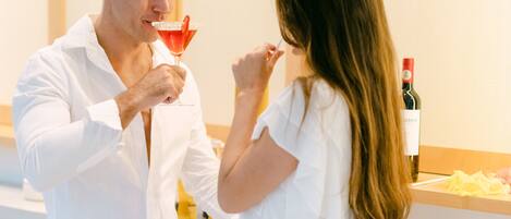 A man and a woman in a white room with a counter and a bottle of wine.