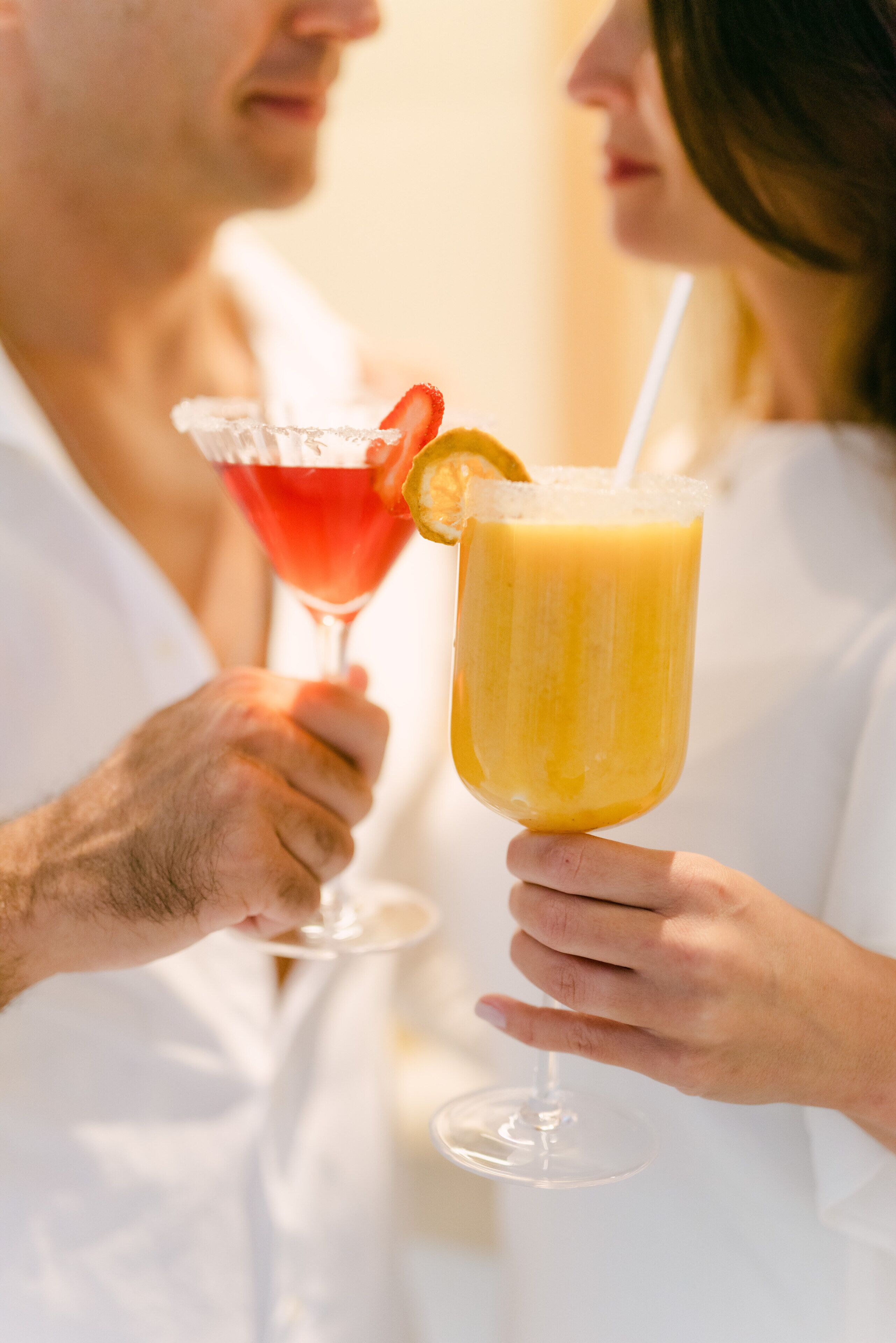 Zwei Personen mit Getränken, eine mit einem roten Cocktail und die andere mit einem gelben Getränk, beide mit Trinkhalmen.