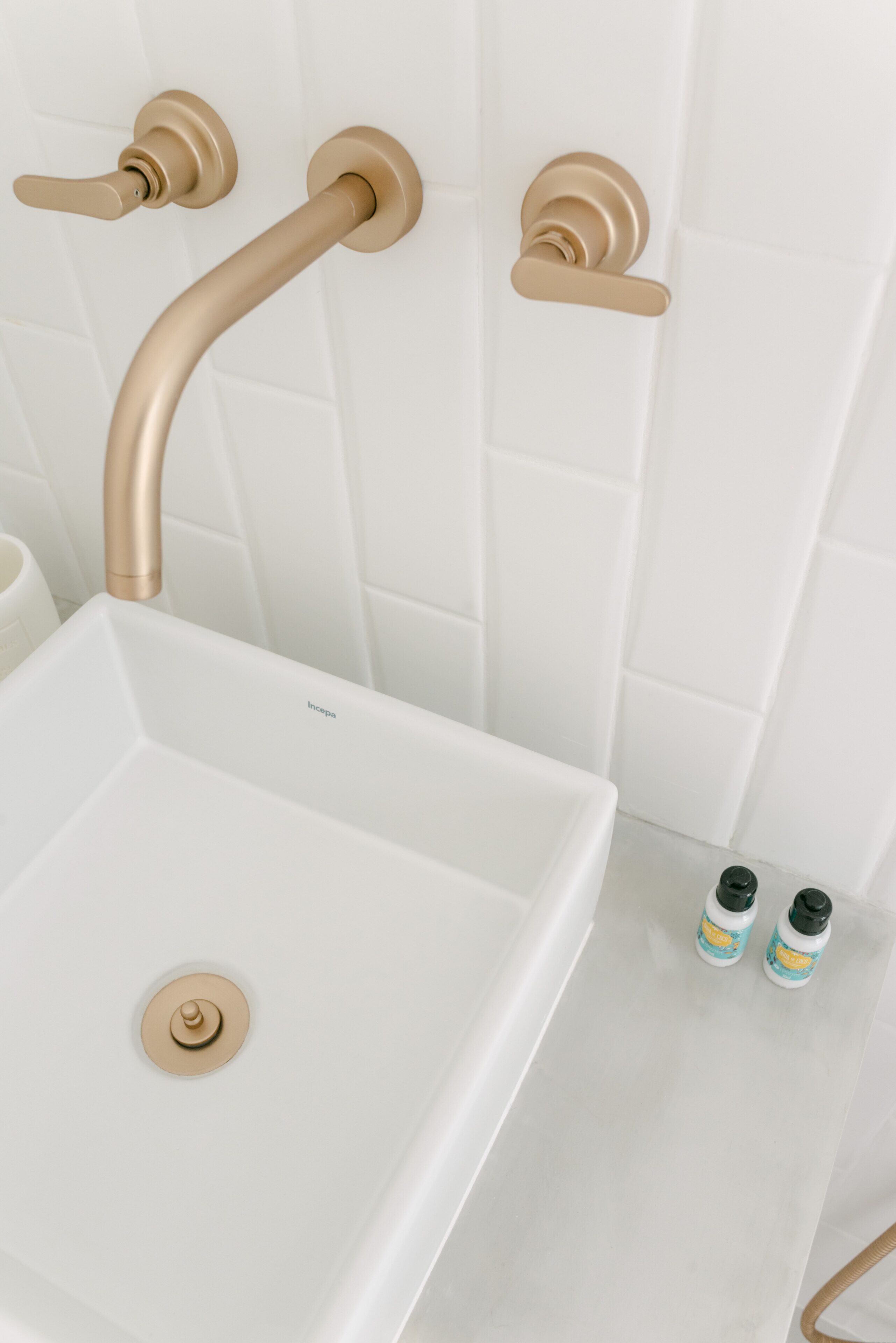 A bathroom with a white sink, gold fixtures, and two toiletry bottles on the floor.