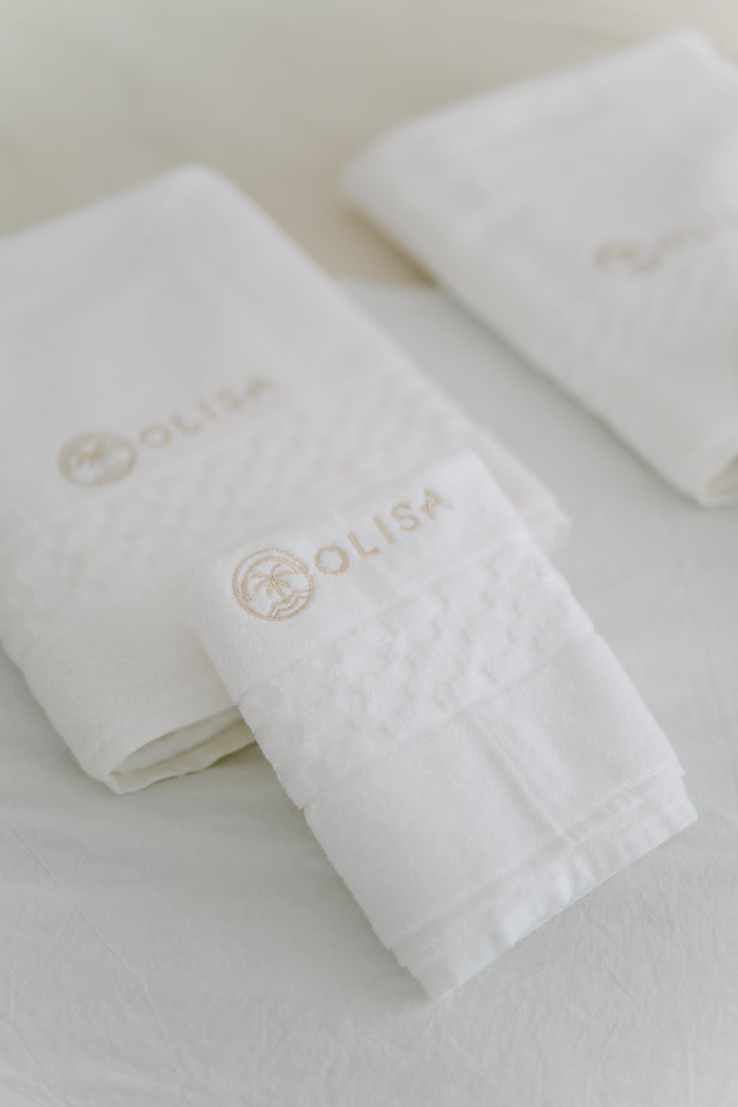 Toalhas brancas dobradas com a marca 'OLISA' em relevo.