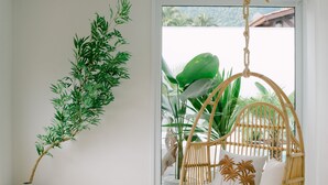 Quarto com uma cadeira suspensa, dois vasos brancos, um tapete tecido e vista para o verde lá fora.