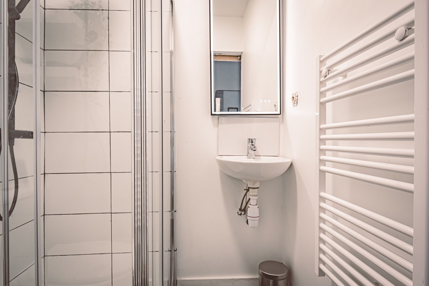 Een badkamer met een douchecabine van glas, een witte wastafel en een handdoekhouder.