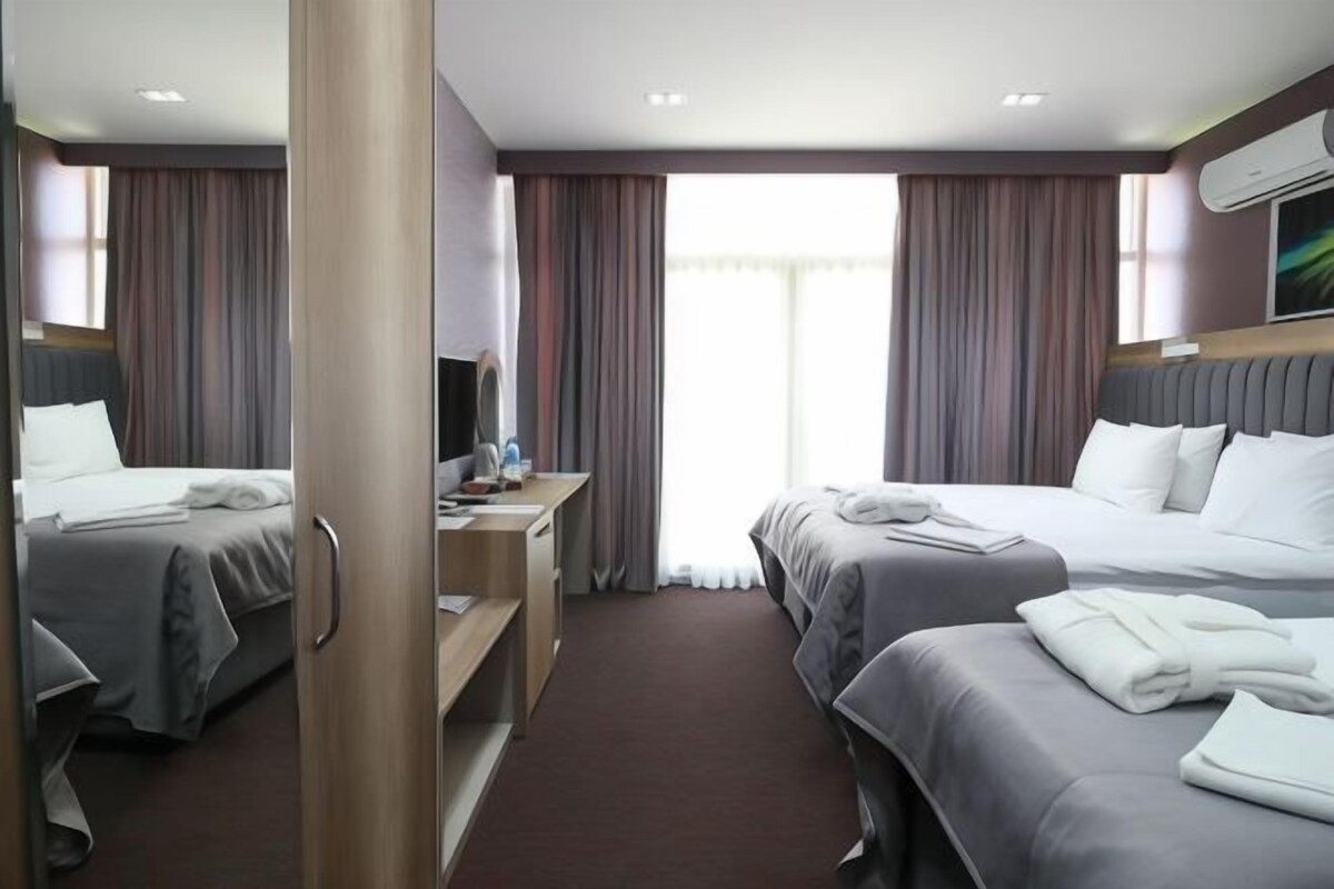 Una habitación de hotel con dos camas, un escritorio y un ventanal con cortinas.