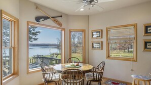 A dining area with a round table and chairs, large windows with lake views, and a ceiling fan. - The Sweet Seclusion Cottage with 100 feet of Private frontage Pickerel Lake! (Alanson)