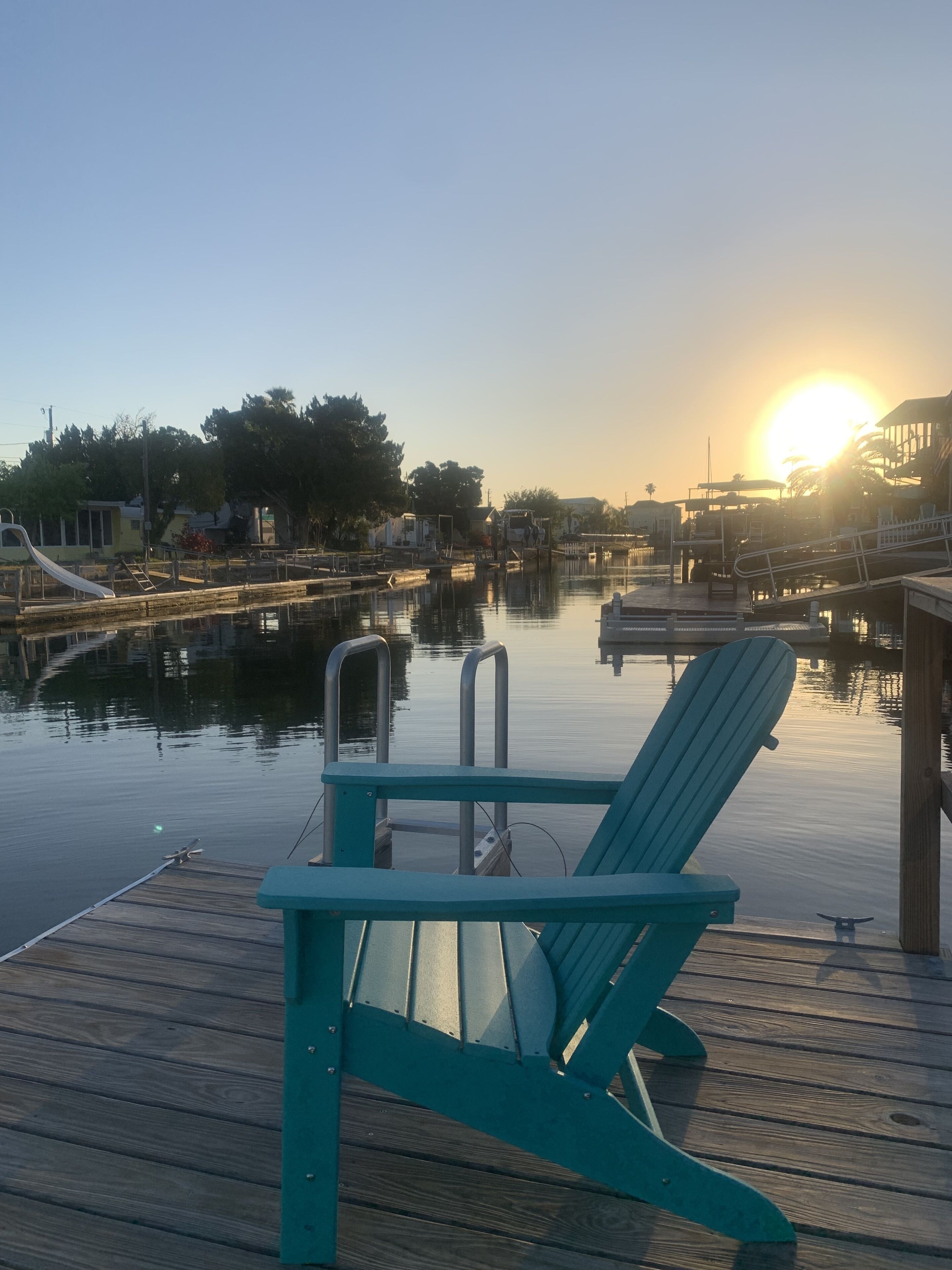 A wooden dock with a teal chair and a small boat docked.