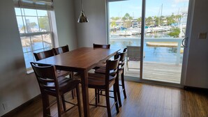 Un comedor con mesa y sillas de madera, amplias ventanas y vistas a un puerto deportivo.