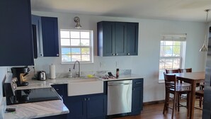 Una cocina moderna con armarios azul oscuro, un lavavajillas de acero inoxidable y una mesa de comedor de madera con sillas.