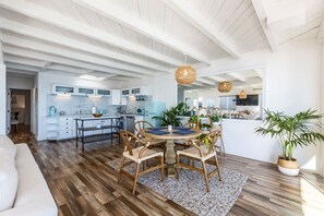 A spacious kitchen with white cabinets, a dining area with a round table, and a living room with a sofa.