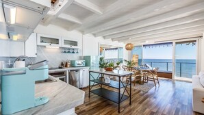 A modern kitchen with a dining area, large windows, and a view of the sea. - Casa Penelope by Oraklus (Malibu)