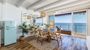 A dining area with a table and chairs, a refrigerator, potted plants, and a view of the sea. - Casa Penelope by Oraklus (Malibu)