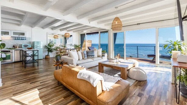 A spacious living area with a sofa, coffee table, and dining table, a kitchen with modern appliances, and large windows offering a view of the sea. - Casa Penelope by Oraklus (Malibu)