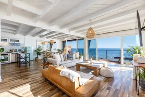 A spacious living area with a sofa, coffee table, and dining table, a kitchen with modern appliances, and large windows offering a view of the sea. - Casa Penelope by Oraklus (Malibu)