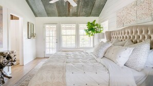 Une chambre avec un grand lit, un ventilateur de plafond et une vue sur l’extérieur par les fenêtres.
