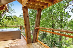 Une terrasse en bois dotée d’un jacuzzi, entourée d’une balustrade en bois et d’une clôture en fil de fer, et offrant une vue sur une zone boisée.