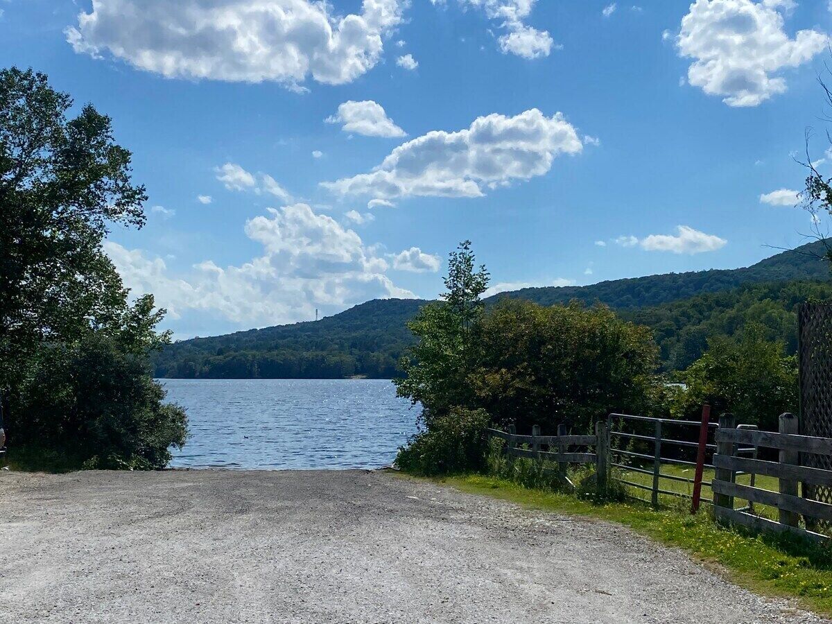 A gravel path leading to a lake with a wooden fence on the right and trees on the left.