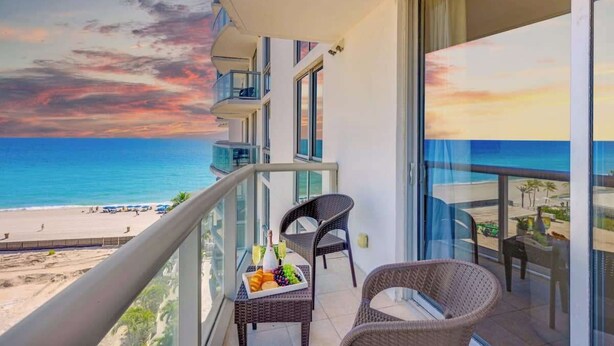 A balcony with wicker furniture, a fruit basket, and a view of the beach and ocean during sunset.
