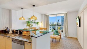 A modern kitchen with a glass island, pendant lights, and a view of the cityscape through large windows.