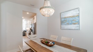 A dining area with a wooden table, white chairs, a chandelier, and a painting on the wall. - Discover why Serenity is a popular family vacation spot in Perdido Key! (Perdido Key)