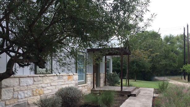 A stone wall with a small garden area, a concrete pathway, and a wooden pergola structure. - 5 minutes to downtown! Family home with fenced yard, deck, wooded lot (Austin)