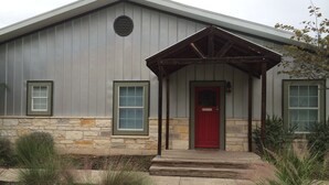 A modern building with a red door, stone foundation, and a covered porch. - 5 minutes to downtown! Family home with fenced yard, deck, wooded lot (Austin)