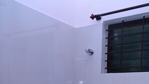 Un baño pequeño con inodoro, ducha y una ventana con barrotes.