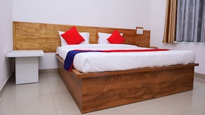 Una cama de madera con ropa de cama blanca y almohadas rojas, una mesita de noche blanca y una ventana con cortinas.