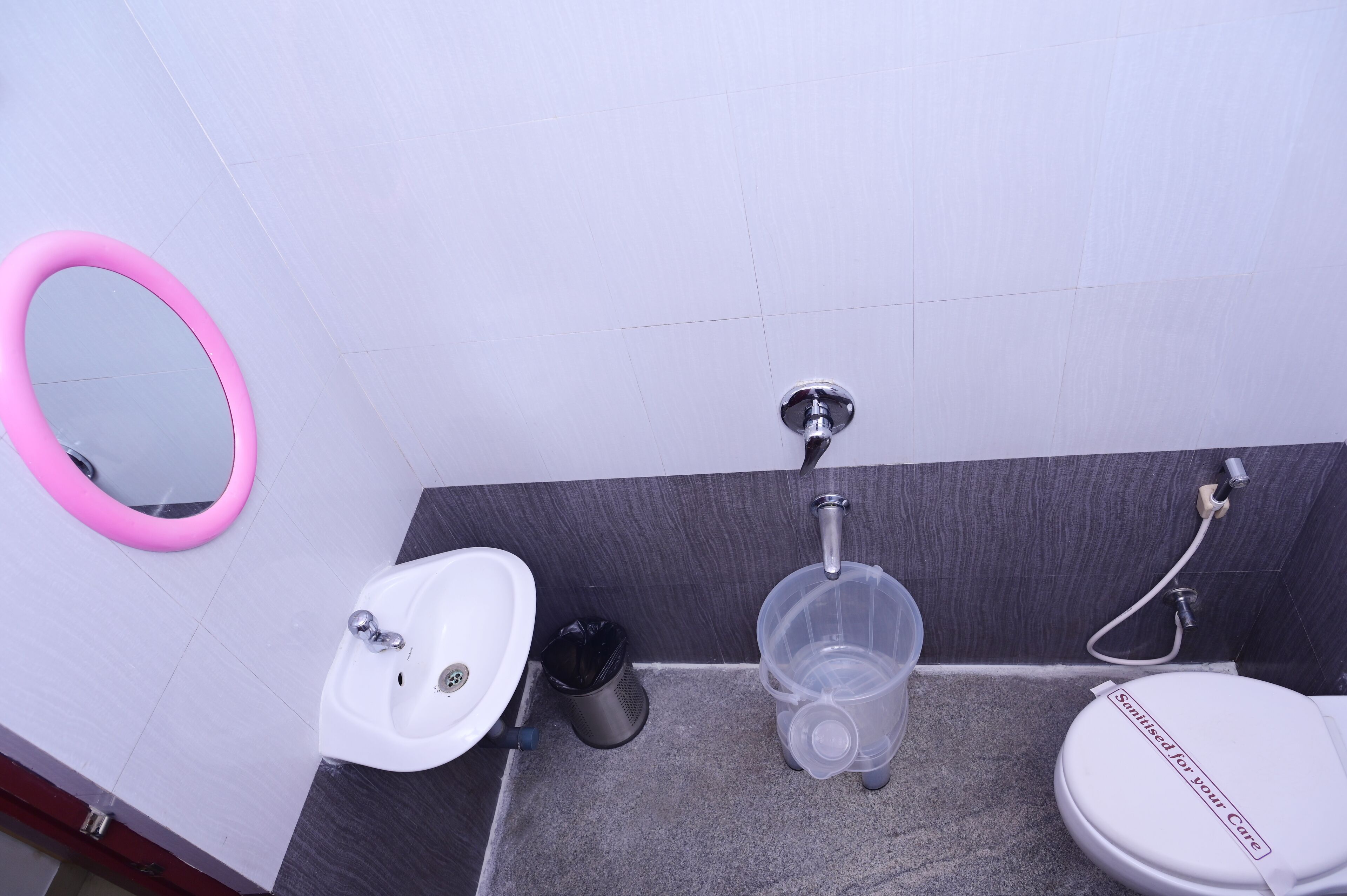 A bathroom with a white sink, a pink-framed mirror, a toilet, and a shower head.