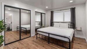 Une chambre à coucher moderne avec un grand lit, une table de chevet, un miroir et une porte coulissante donnant sur une salle de bain.