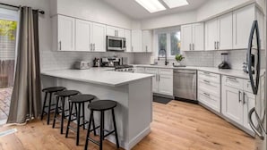 Une cuisine moderne avec des meubles blancs, un îlot central doté de tabourets, un four à micro-ondes et un lave-vaisselle.