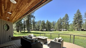 Eine Holzterrasse mit Gartenmöbeln und Blick auf einen Golfplatz, ferner blauer Himmel.