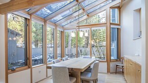 Ein geräumiges Zimmer mit großem Holztisch und Stühlen, einer Glasdecke und großen Fenstern mit Blick ins Freie.